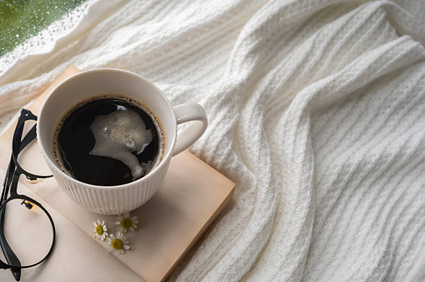 istock A white mug of coffee and spectacle put on book with blanket when rain drop on window. 2227633354