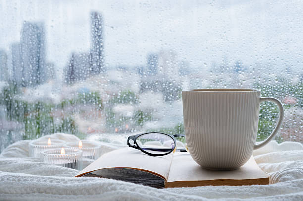istock A coffee mug and spectacles put on book with candle on blanket when rain drop on window. 2227633356