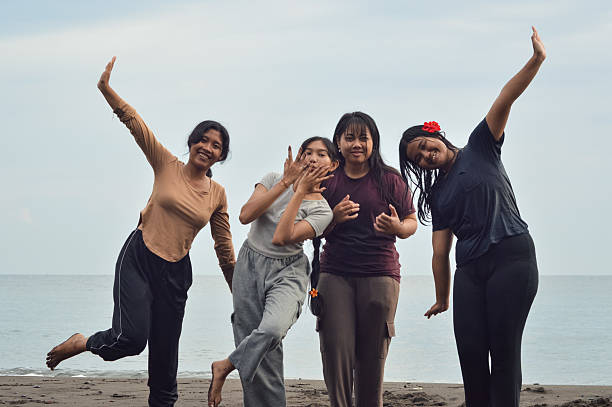 A cheerful group of teenage girls pose confidently for a photo on the shoreline with sparkling waves behind them.