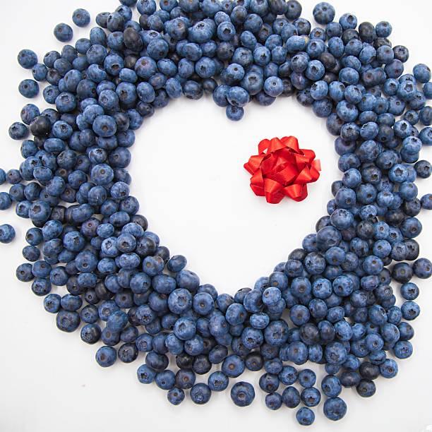 Blueberries arranged in a heart shape with red ribbon on white background