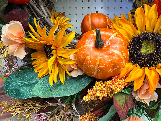 Stock photo showing close-up view of autumnal  wreath decoration, background of artificial sunflower heads, fake berries and plastic, orange pumpkins.