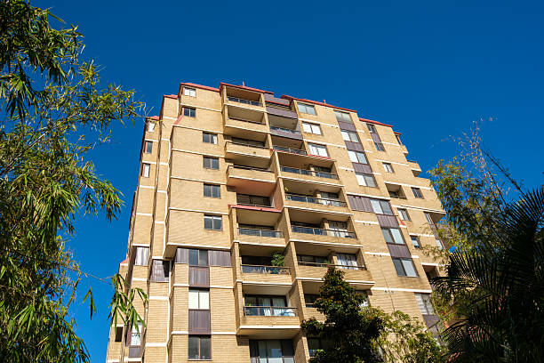 Beige brick apartment building with clear blue sky and trees.