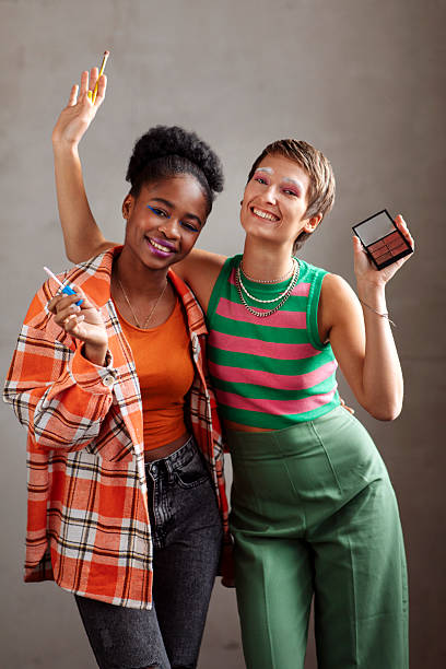 Portrait of a two diverse young gen z unique girls, smiling and holding makeup tools indoors