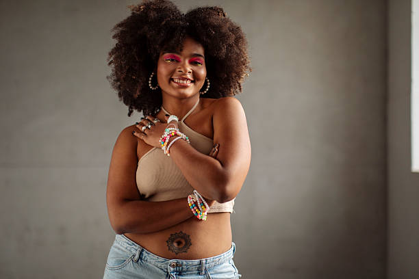 Portrait of smiling gen z black girl with an afro hairstyle smiles at camera in brightly in a photography studio setting; The scene celebrates self-expression and individuality
