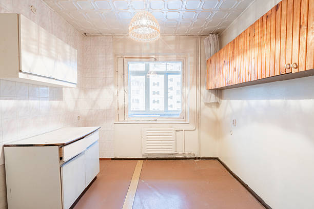 Empty and basic kitchen showcasing old white cabinets, tiled walls, a single sink, and natural lighting through a window. Old Retro Soviet Style Home Kitchen Interior