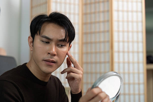 istock Self-Care Routine: Young Man Applying Skincare in Front of Mirror 2227656754