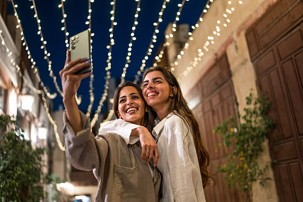 Two Smiling Female Friends Taking a Selfie in Al Balad Under String Lights