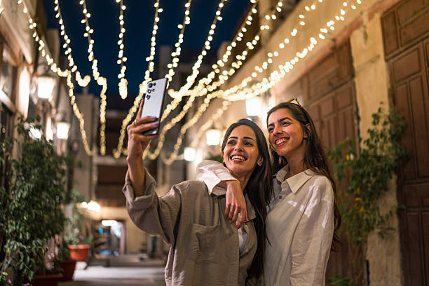 istock Smiling Female Friends Taking a Selfie in Al Balad Under Festive String Lights at Night 2227658629