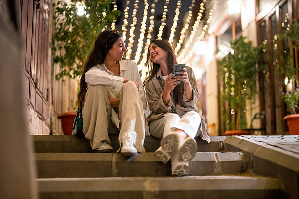 istock Young Women Relaxing on Steps in Al Balad Under String Lights with Smartphone 2227658648
