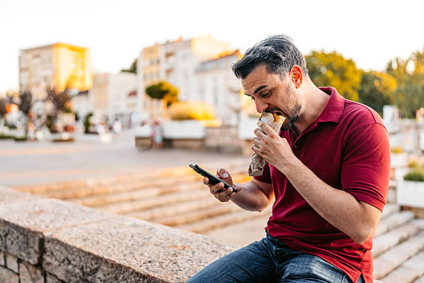 istock Mid-Adult Man Using Phone While Eating A Pastry On The Quayside 2227662537