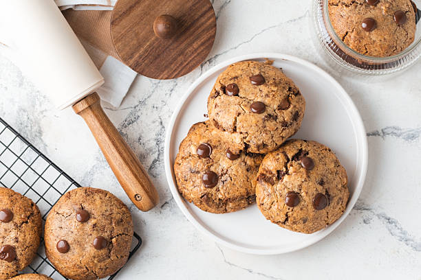 istock Fresh chocolate American chip cookies with nuts and chocolate drops on white marble background. Flat lay of cookies with stylish cutlery and pastry chef accessories. Recipe of homemade cookies concept 2227664966