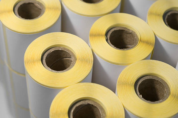 istock Rollers with a white self-adhesive label for printing labeling information. Ribbon with white label on cardboard spools. Products of the printing house. Selective focus 2227665328