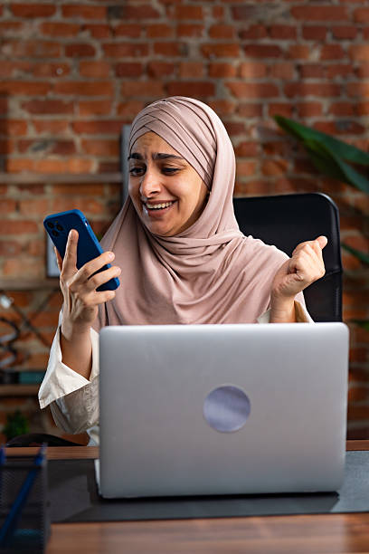 istock Smiling Woman in Hijab Using Smartphone at Modern Workspace 2227667128