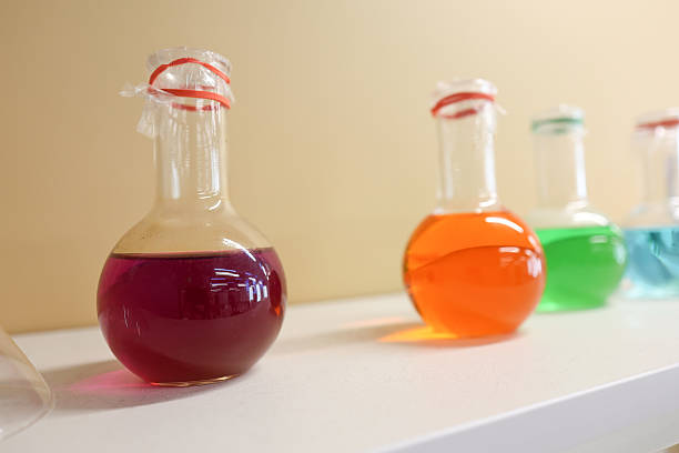 Group of children in lab coats and gloves performing chemistry experiments using glassware, hot plates, scales, and liquid reagents in a modern laboratory setting.