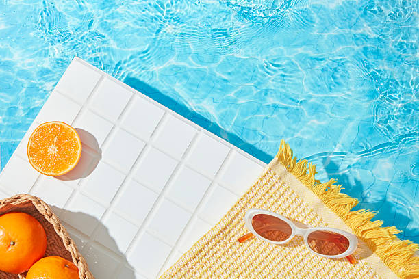istock Oranges, sunglasses, and straw bag on a white tile edge pop against vibrant pool blue. A sunny summer scene perfect for product mockups in travel skincare, natural citrus beauty, or sun protection. 2227669429