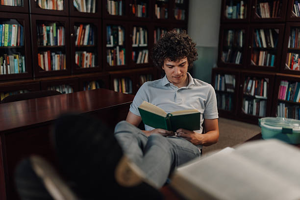 istock Young man reading a book in the library with feet up 2227669612