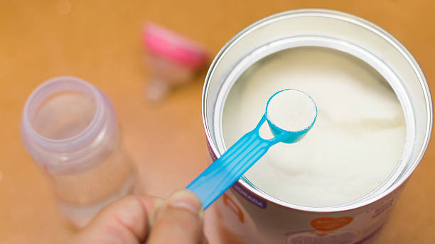 Mother preparing baby formula in kitchen with powdered milk