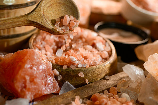 Close up shot of variety of types and sizes of himalayan salt, arranged on a table in a wooden and a glass jars and bowls, prepared for a studio shot. Healthy lifestyle, spa, bathtub, healthy eating.