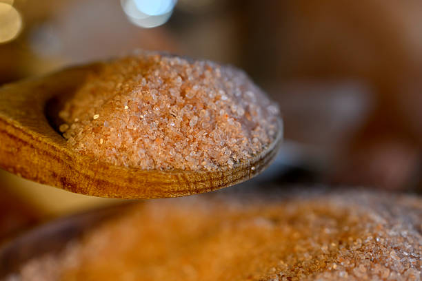 Extreme close up shot of a himalayan salt on a wooden spoon and a bowl. Food preparing, salt seasoning, food ingredient, nutritional supplement. No people.