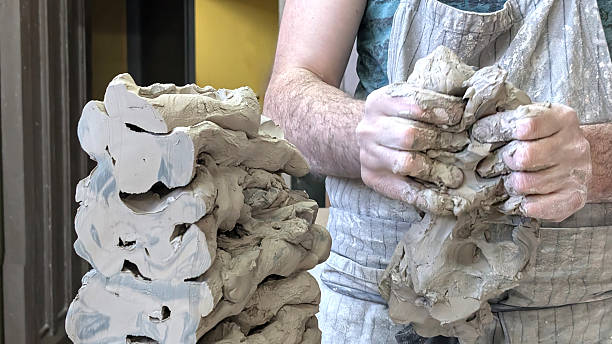 istock Artist kneads the clay before sculpting in a studio setting during daytime. Stacks of unfinished clay nearby. Craftsmanship, artisanal work and creative processes concept. 2227692613