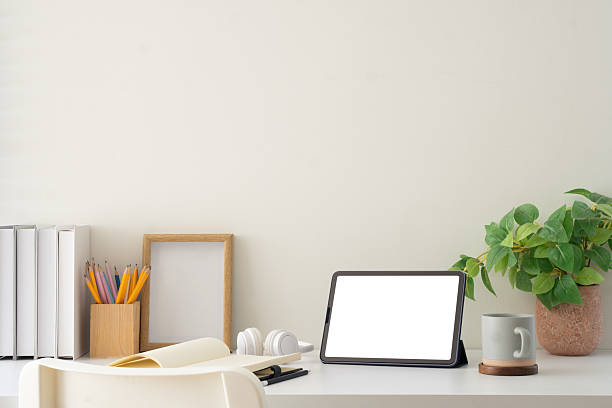 istock Minimal white desk featuring digital tablet with blank screen, notebook, and coffee mug, ready for design insertions. 2227695337