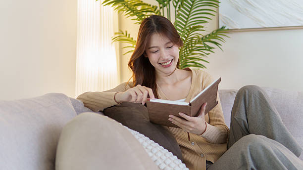 istock Cheerful lady  reading book on couch surrounded by modern home decor and soft lighting. 2227696078