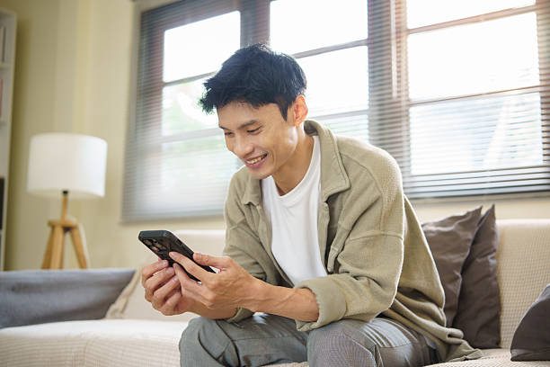 istock Young man sitting on a sofa at home, using a smartphone in a relaxed and cozy. 2227696171