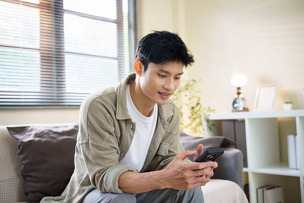 istock Young man sitting on a sofa at home, using a smartphone in a relaxed and cozy. 2227696175
