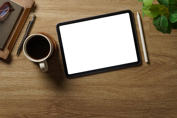 istock Digital tablet with blank screen on wooden desk surrounded by coffee cup and notebook, for app or web design. 2227696207