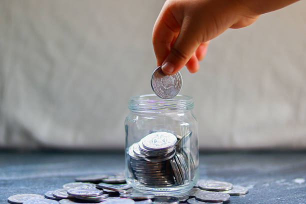 istock Hand holding a coin put in a jar on a table, Saving money concept 2227696369
