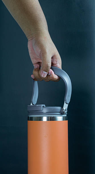 istock Orange tumbler bottle held by its handle, portrait frame on black background, clean and bold hydration concept with modern lifestyle appeal 2227696702