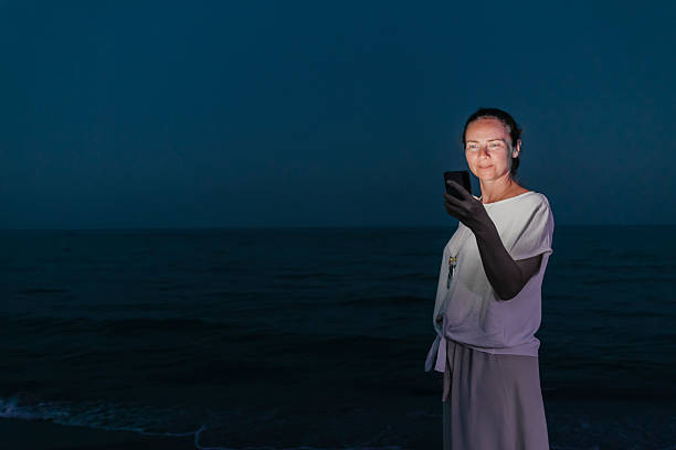 Woman walking down the beach using smart phone while relaxing by the sea at dusk