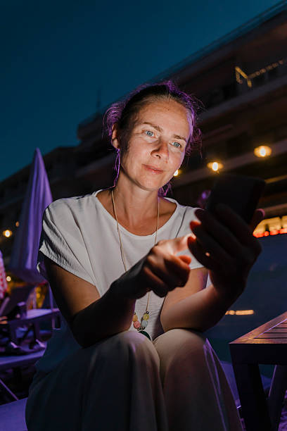 istock Woman sitting on sunbed at the beach using smart phone at dusk 2227698030