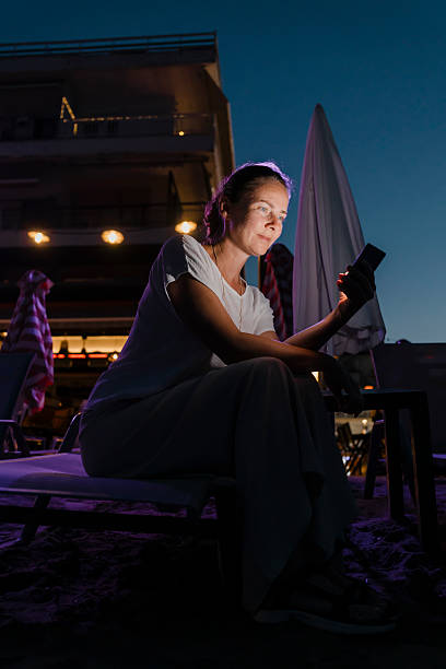 istock Woman sitting on sunbed at the beach using smart phone at dusk 2227698047