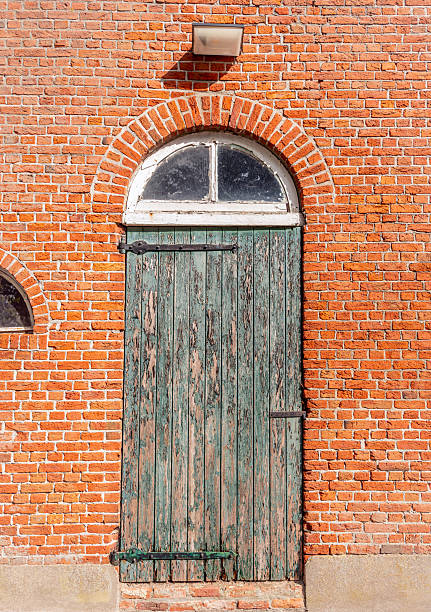 A door with peeling green paint in the brick wall of an old barn. The photo was taken in the outskirts of Breda in the Dutch province of North Brabant.
