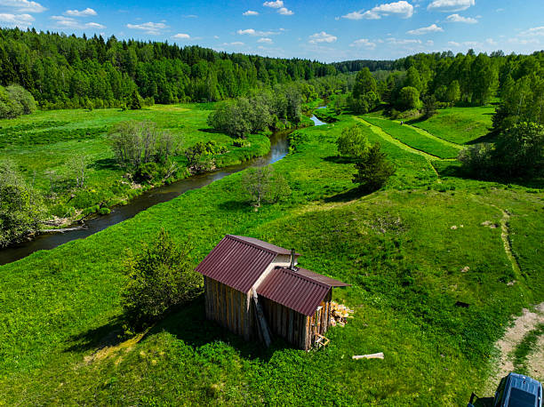 istock Rural cabin by winding river amidst green fields and forests 2227702139