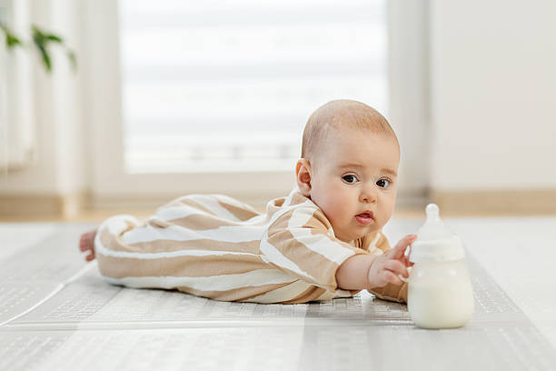 istock Baby lying on floor reaching for milk bottle. 2227702247