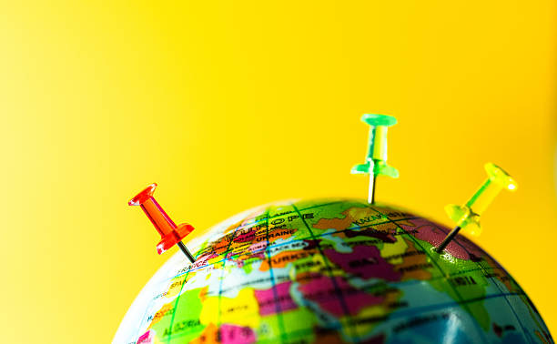 Close up of world globe with three push pins on yellow background
