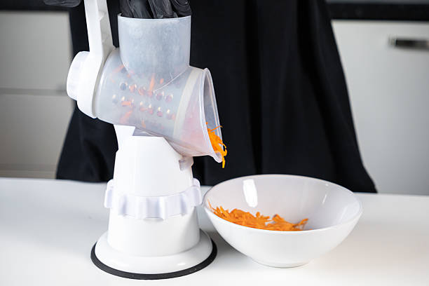 istock Person using a white manual rotary grater to efficiently shred fresh orange carrots into a white bowl, demonstrating practical kitchen food preparation and healthy cooking 2227706929