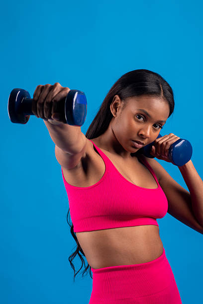 istock Young black woman lifting weights on blue background 2227708983