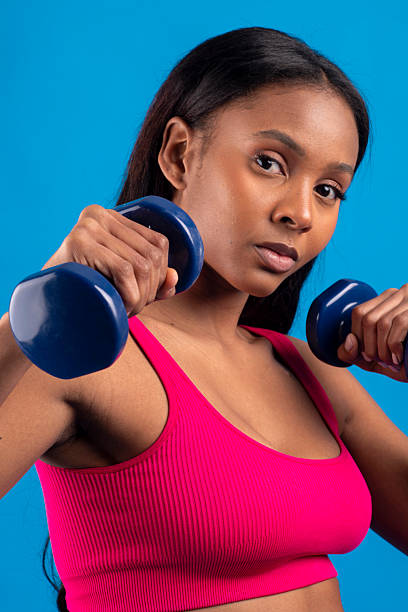 istock Young woman lifting weights on blue background 2227709076