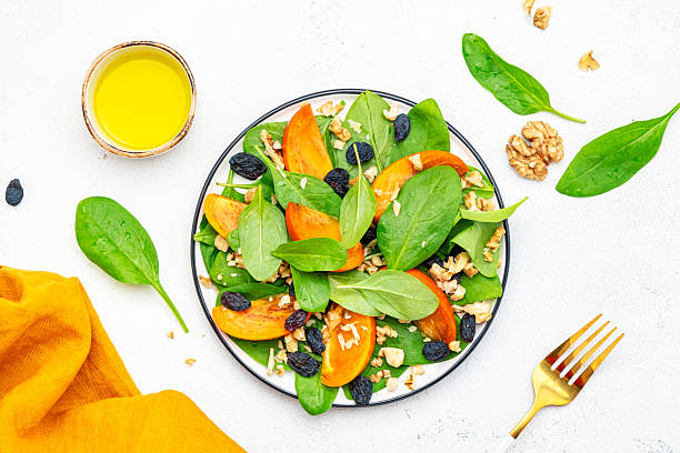istock Yummy persimmon salad with walnuts, raisin and fresh spinach, white background, top view 2227712620