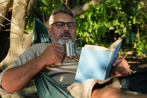 istock Middle-aged man reading, drinking coffee, and camping in the forest 2227713222