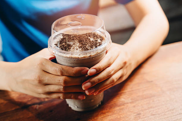 Hands Holding Chocolate Milkshake in Clear Cup on Table