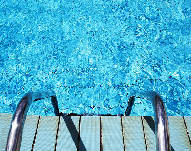 Swimming pool with clear blue water.The bottom of the pool is tiled with light blue color.There are black lines along the bottom of the pool dividing the paths.The water is calm and quiet,there are no people visible in the pool.