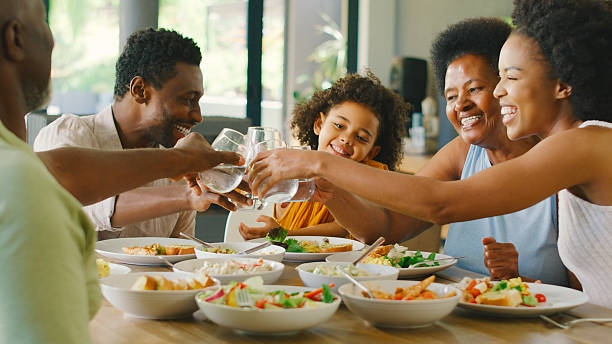 Multi-Generation Family Around Table Doing Cheers With Water Before Serving Food For Meal At Home
