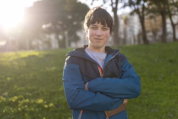 Portrait of a confident male student holding books, smiling with arms folded in a park during golden hour