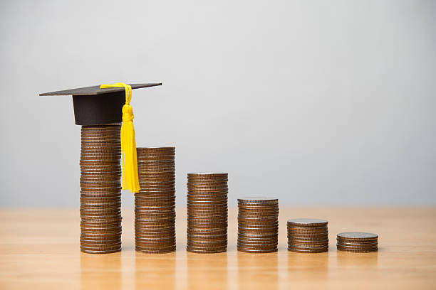 istock Mortarboard or square academic cap and reduce stack coins chart on wooden table with white wall background. 2227719150
