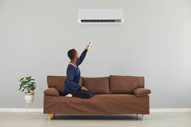 istock Woman on the sofa using a remote control to set the temperature on the air conditioner 2227720806