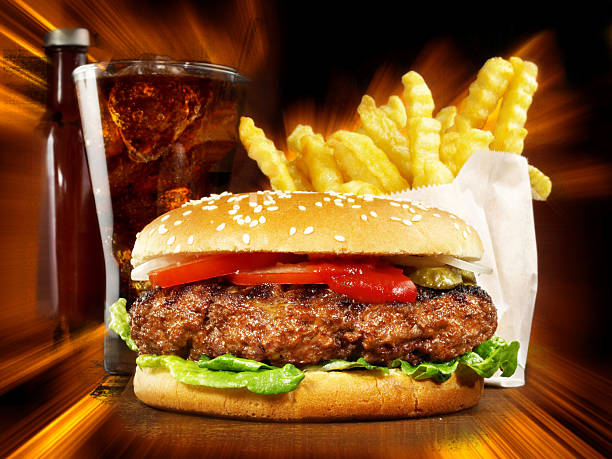 Fresh hamburger in paper wrapping, crispy French fries in carton box and glass bottle of drink isolated on yellow background. Set from fast food restaurant menu. Popular snacks concept